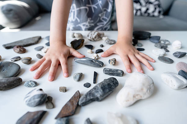 A close-up shot of a child's hands and arranged various stones and rocks of different sizes and colours on a white table.